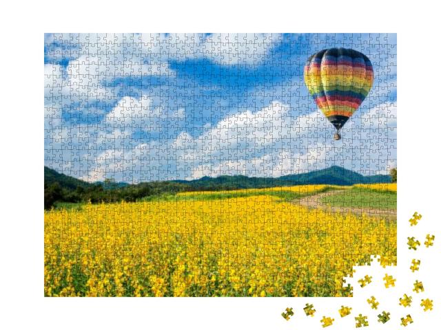 Puzzle 1000 Teile „Heißluftballon über gelben Blumenfeldern, im Hintergrund ein Mittelgebirge“