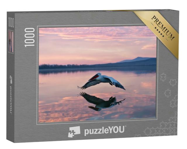 Puzzle 1000 Teile „Schweben über dem Wasser: Pelikan im Sonnenaufgang“